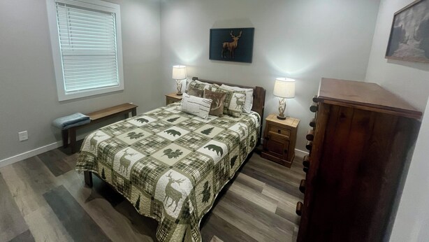 A bedroom with a bed, two bedside tables, a bench, a window with blinds, and a wall-mounted lamp. - 3-bedroom cabin close to Downtown Clayton with a Mountain feel. (Clayton)