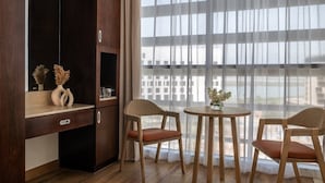 A room with a wooden desk, two chairs, a small table with a vase, and a large window with sheer curtains. - Yas Plaza Circuit by IHG (Abu Dhabi)