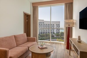Una habitación de hotel moderna con un sofá, una mesa de centro redonda, una lámpara y un televisor.