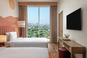 A hotel room with two beds, a TV, a desk, and a view of a cityscape. - Yas Plaza Circuit by IHG (Abu Dhabi)