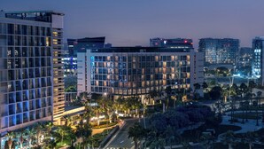 Un hotel moderno con varios pisos, un vestíbulo bien iluminado y un área exterior ajardinada con palmeras.