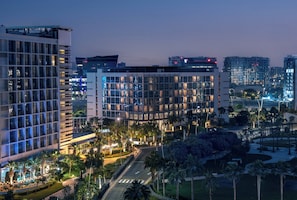 Un hôtel moderne à plusieurs étages, doté d’un hall d’entrée bien éclairé et d’un espace extérieur aménagé avec des palmiers.