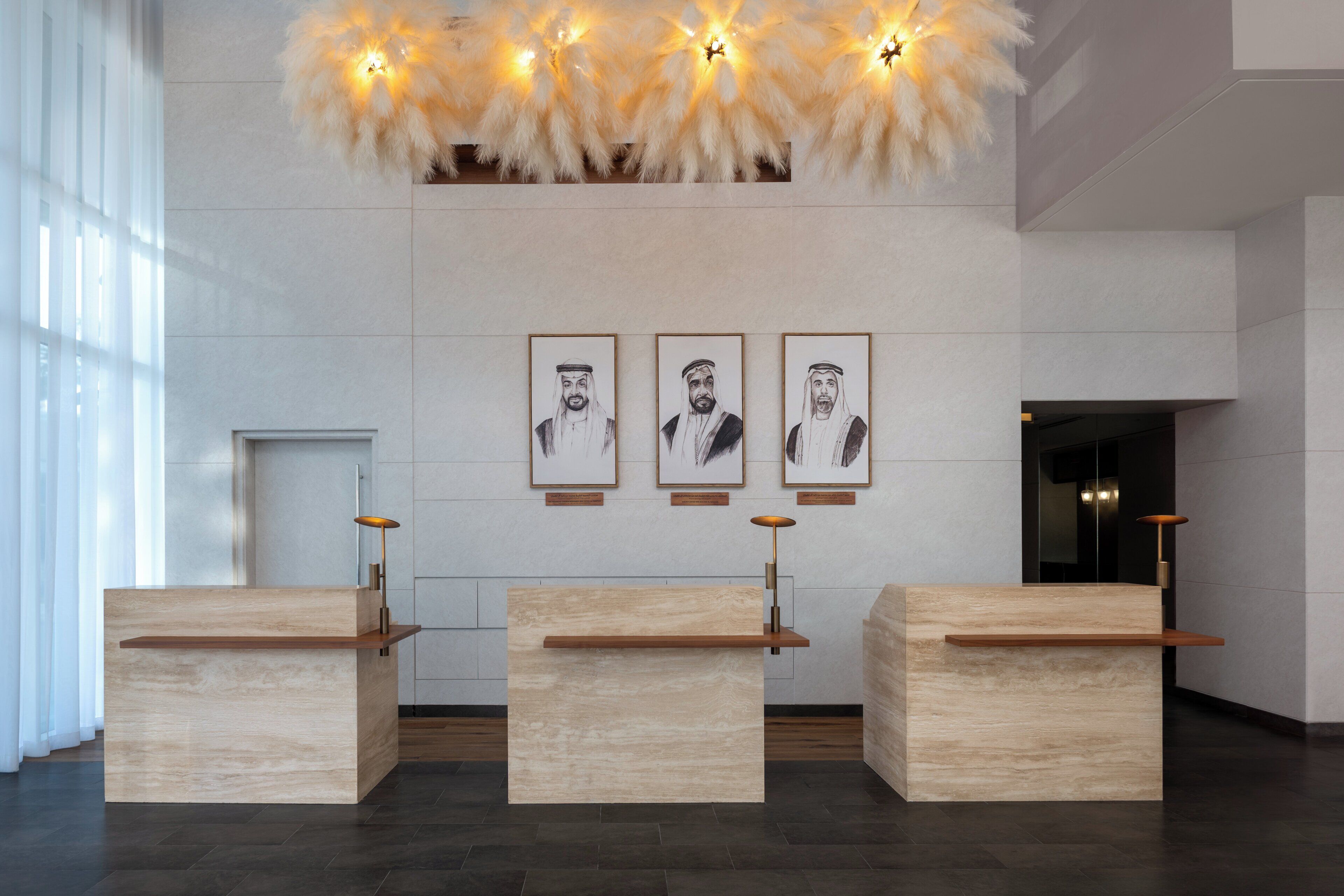 A reception area with three wooden reception desks, a wall-mounted light fixture, and three framed portraits above the desks.
