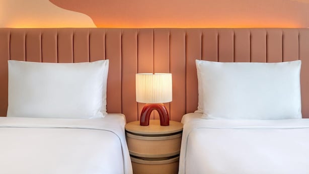 A hotel room with a bed, two pillows, a nightstand with a lamp, and a wall with a unique design. - Yas Plaza Circuit by IHG (Abu Dhabi)