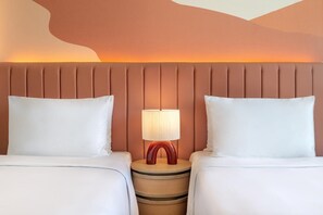 Habitación de hotel con una cama, dos almohadas, una mesita de noche con una lámpara y un diseño único en la pared.