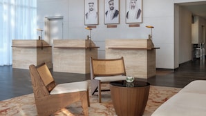 A reception area with wooden reception desks, a rattan chair, a round wooden table, and framed portraits on the wall. - Yas Plaza Circuit by IHG (Abu Dhabi)