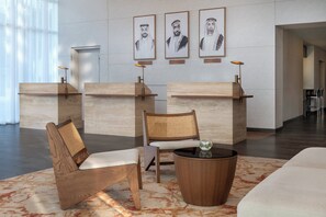 Un área de recepción con mostradores de madera, una silla de ratán, una mesa redonda de madera y retratos enmarcados en la pared.