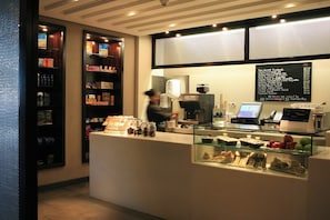 A cafe interior with a counter, menu board, and shelves with snacks. - Yas Plaza Circuit by IHG (Abu Dhabi)