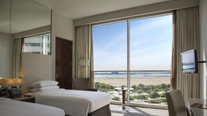 Habitación de hotel con una ventana grande, una cama, un escritorio y un televisor.