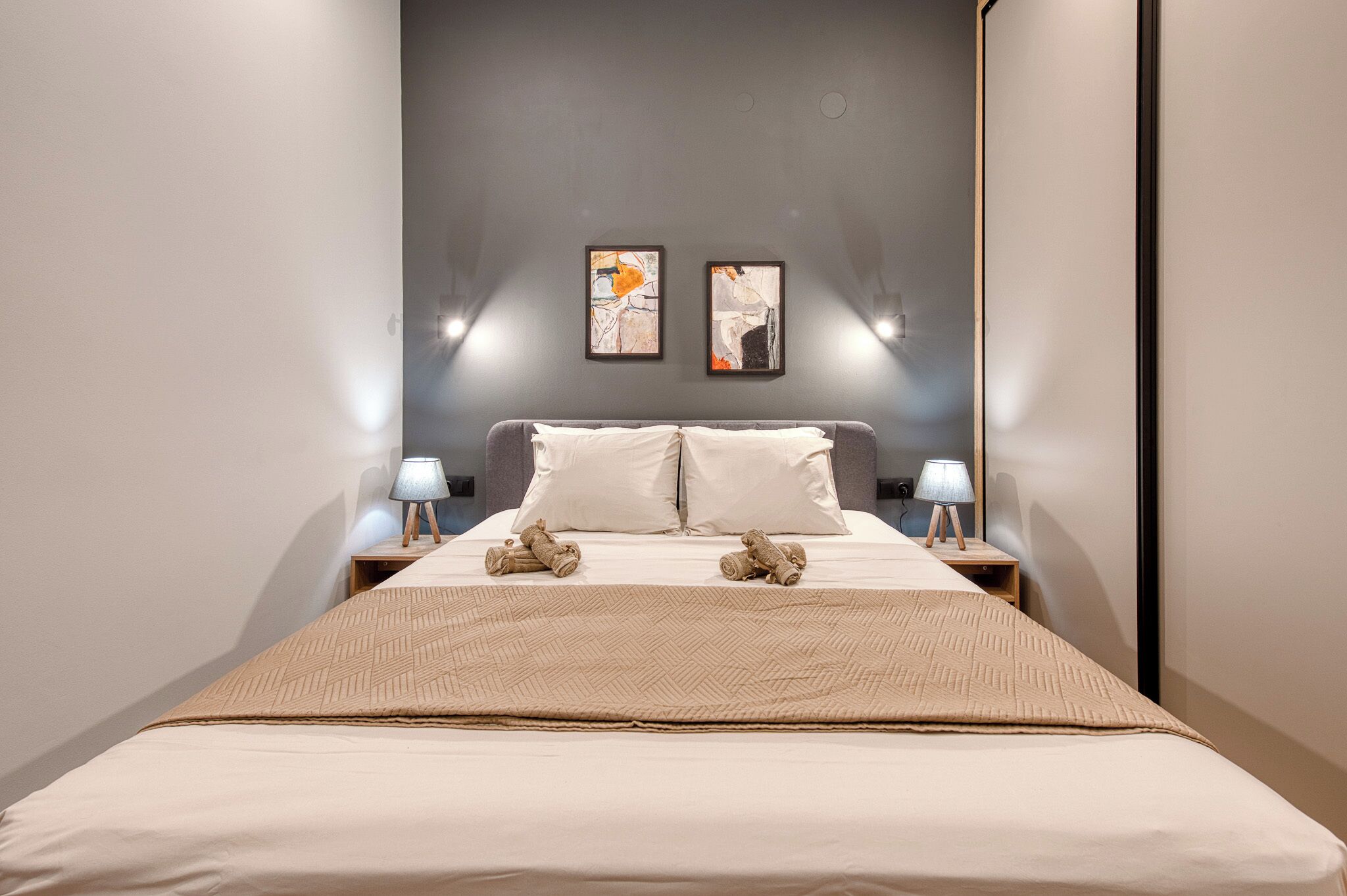 A hotel room with a bed, two nightstands, two wall-mounted lamps, and two framed artworks.