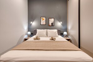 Une chambre d’hôtel comprenant un lit, deux tables de chevet, deux lampes fixées au mur et deux œuvres d’art encadrées.
