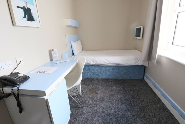 A small hotel room with a desk, chair, bed, and a window.
