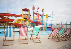 Un parque acuático con piscina, toboganes coloridos y sillas de playa.