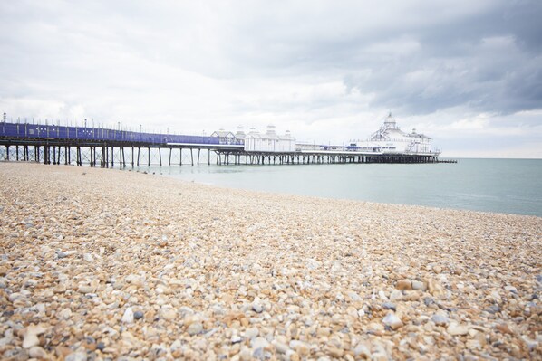 A pebbled beach with a pier extending into calm waters, a white building with a dome, and a cloudy sky. - Citrus Hotel Eastbourne (Eastbourne)