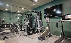 Ein Fitnessstudio mit unterschiedlichen Trainingsgeräten, darunter Kurzhanteln, ein Kraftgerät und ein Crosstrainer.