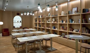 Una biblioteca con varias mesas y sillas, estanterías de madera y un amplio ventanal de arco.