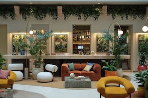 A modern lobby with a sofa, chairs, a coffee table, and a bar area with plants and lighting.