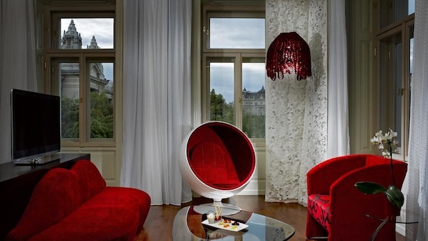 A modern living room with a red sofa, a red armchair, a glass coffee table, and a television on a stand. - Verno House Budapest, Vignette Collection, an IHG Hotel (Budapest)
