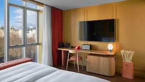 A hotel room with a bed, a desk with a flat-screen TV, a chair, a red telephone, a small speaker, and a vase with dried plants. - Verno House Budapest, Vignette Collection, an IHG Hotel (Budapest)