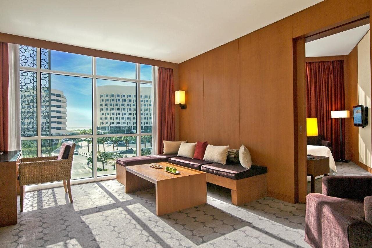 A hotel room with a large window, a sofa, a coffee table, and a chair.