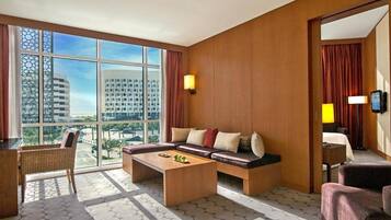 A hotel room with a large window, a sofa, a coffee table, and a chair.