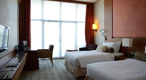 A hotel room with a desk, two beds, a chair, and a large window. - Yas Plaza Marina by IHG (Abu Dhabi)