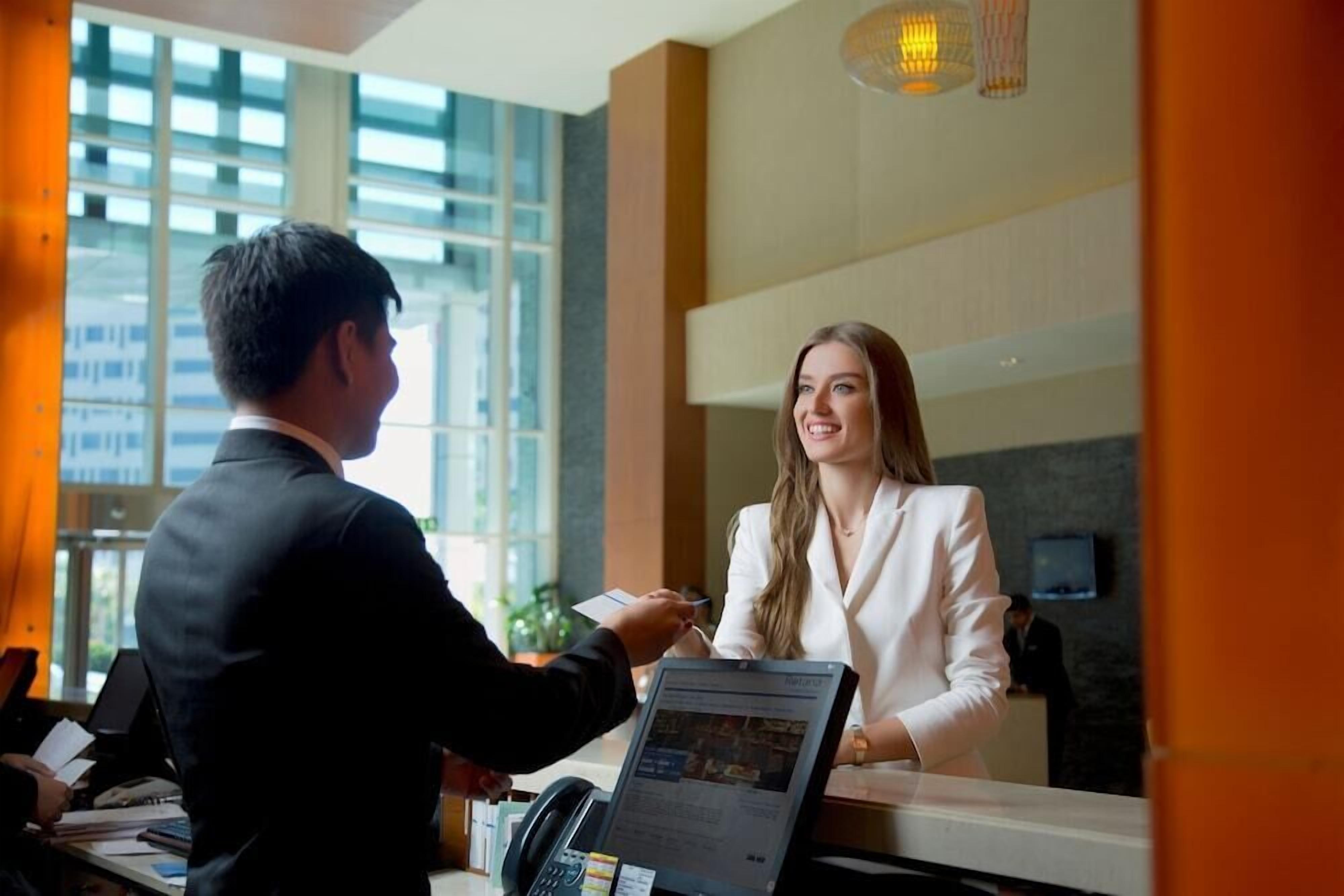 A reception desk with a computer monitor displaying a webpage, a telephone, and a person seated at the desk.