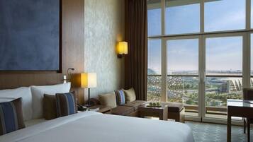 Habitación de hotel con una cama grande, un sofá, una mesita y vistas a la ciudad a través de amplios ventanales.