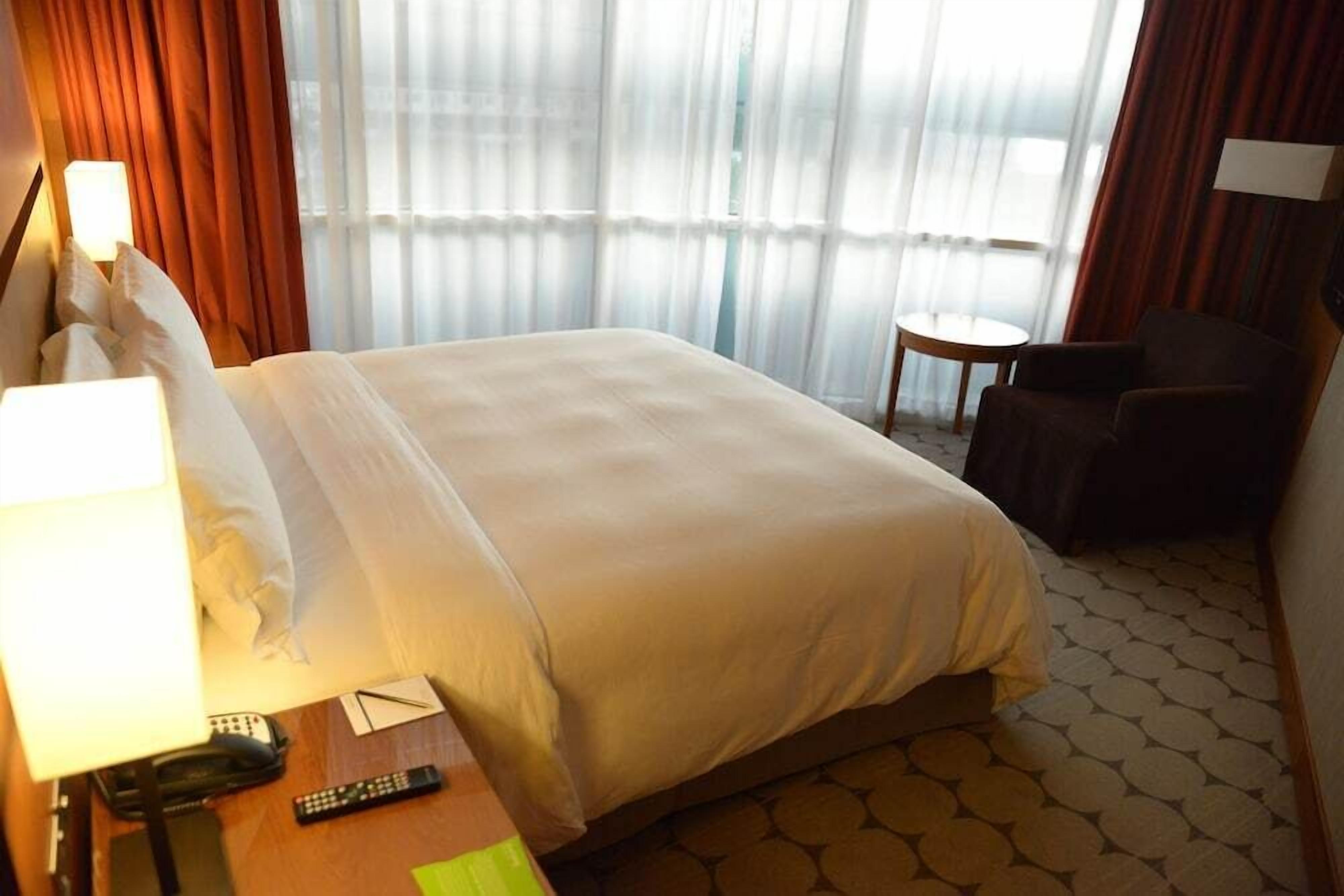 Une chambre d’hôtel avec un lit, une table de chevet avec une lampe, une télécommande, une chaise et une petite table.