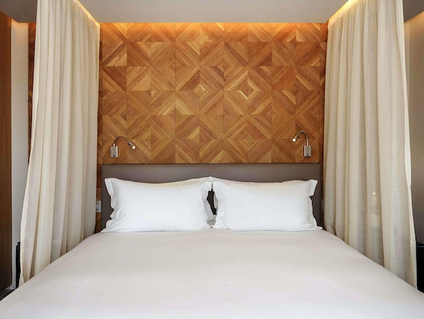 A hotel room with a bed, white curtains, a geometric patterned headboard, and two wall-mounted lamps. - Sofitel Marrakech Palais Imperial and Spa (Marrakech)