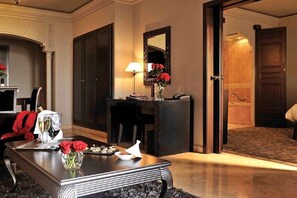 A hotel room with a dining table set with a bottle of champagne, glasses, and a vase of flowers. There is a mirror on the wall and a door leading to another room. - Sofitel Marrakech Palais Imperial and Spa (Marrakech)