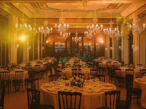 A banquet hall with round tables set for dining, chandeliers hanging from the ceiling, and a view through large windows. - Sofitel Marrakech Palais Imperial and Spa (Marrakech)