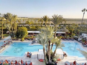 A pool area with two swimming pools, palm trees, lounge chairs, and a view of the surrounding landscape. - Sofitel Marrakech Palais Imperial and Spa (Marrakech)