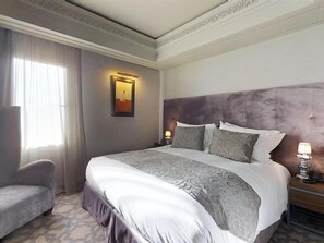 Habitación de hotel con una cama grande, una silla, una mesita de noche y un cuadro en la pared.