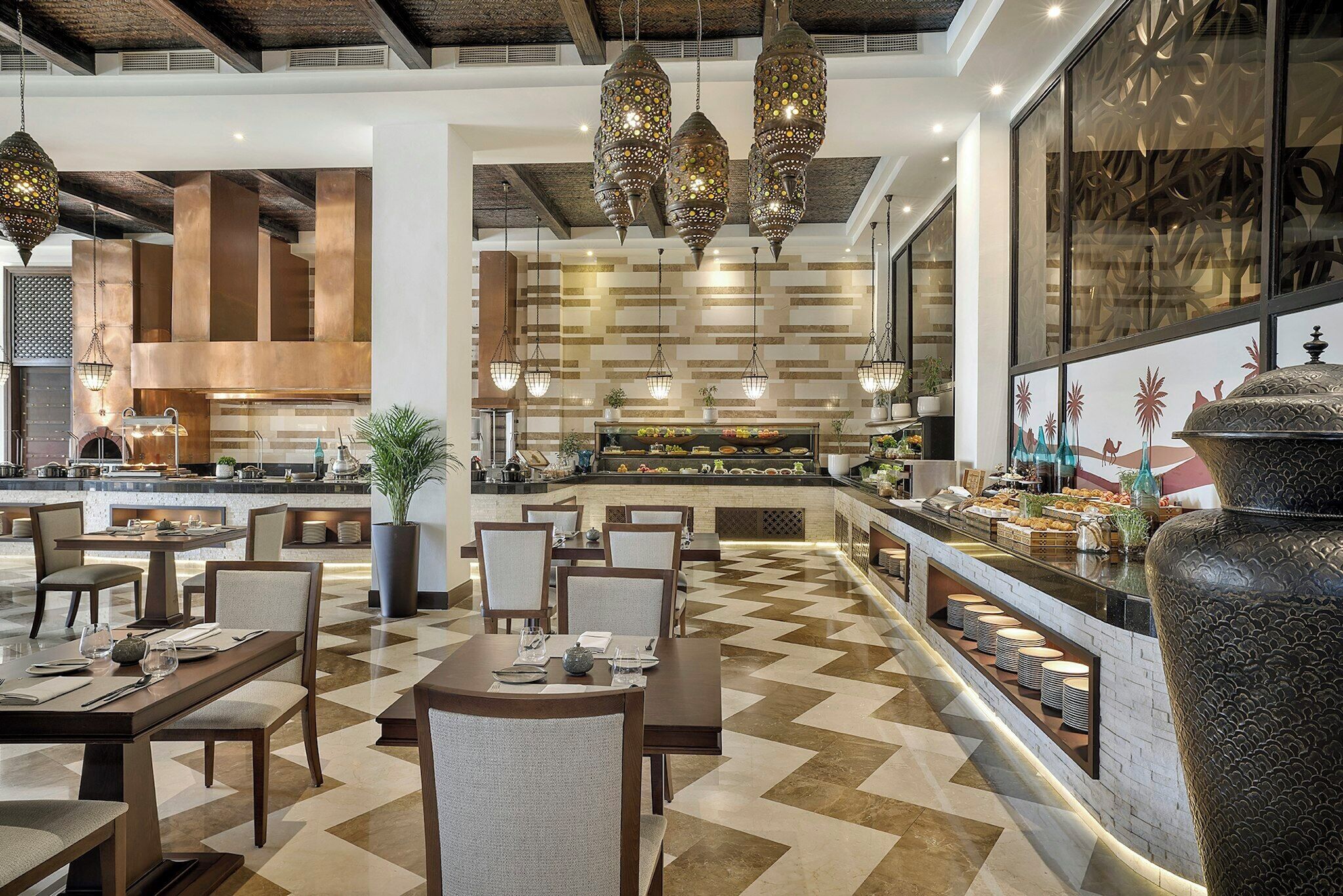 Un restaurante con una decoración moderna, que cuenta con una zona de buffet central, varias mesas de comedor y lámparas colgantes.