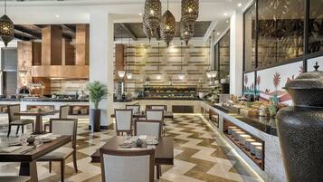 Un restaurante con una decoración moderna, que cuenta con una zona de buffet central, varias mesas de comedor y lámparas colgantes.