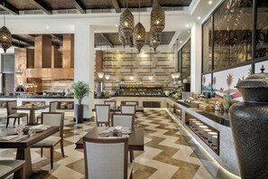 Un restaurante con una decoración moderna, que cuenta con una zona de buffet central, varias mesas de comedor y lámparas colgantes.