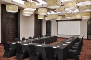 A conference room with a long table, chairs, and a projector screen. - Aldhafra Resort, Vignette Collection, an IHG Hotel (Madinat Zayed)