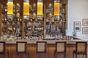 Zona de bar con paneles de madera, varias botellas de licor y taburetes.