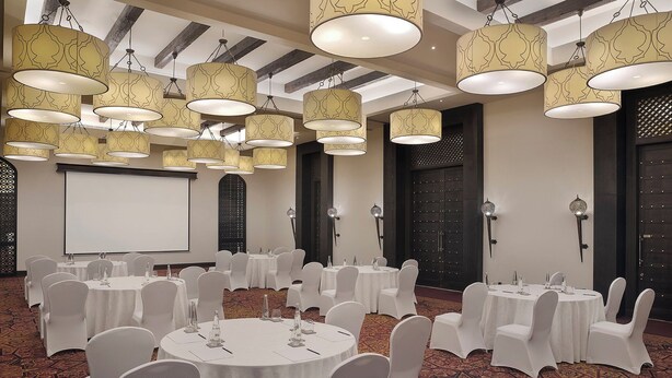 A conference room with multiple round tables, white chairs, and hanging lamps. - Aldhafra Resort, Vignette Collection, an IHG Hotel (Madinat Zayed)