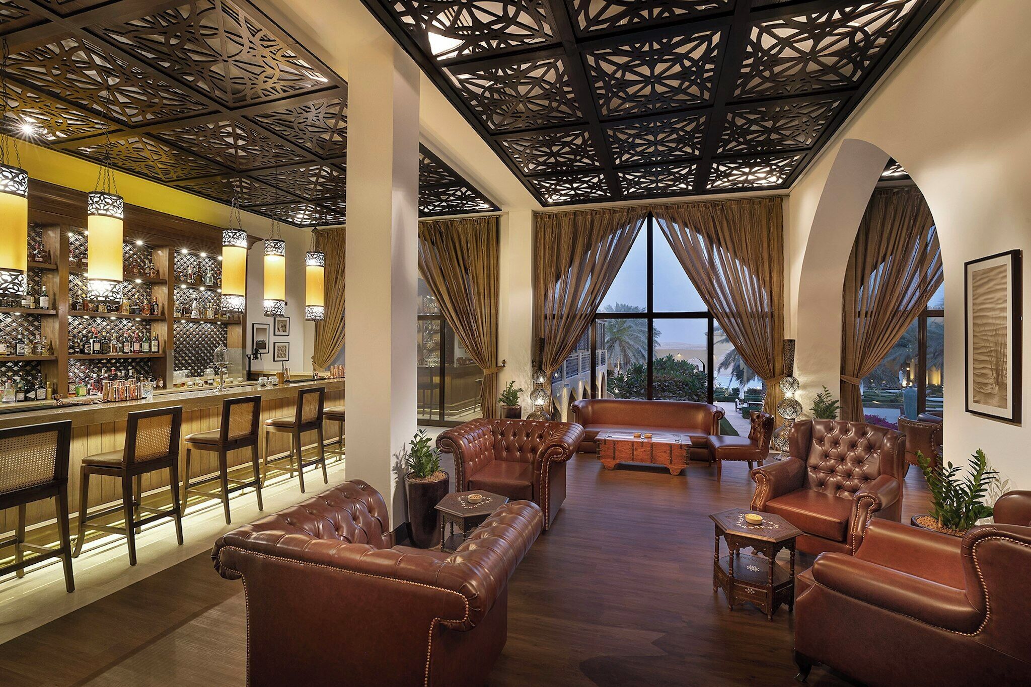A spacious lobby with leather sofas, a bar area with bottles, and a decorative ceiling.