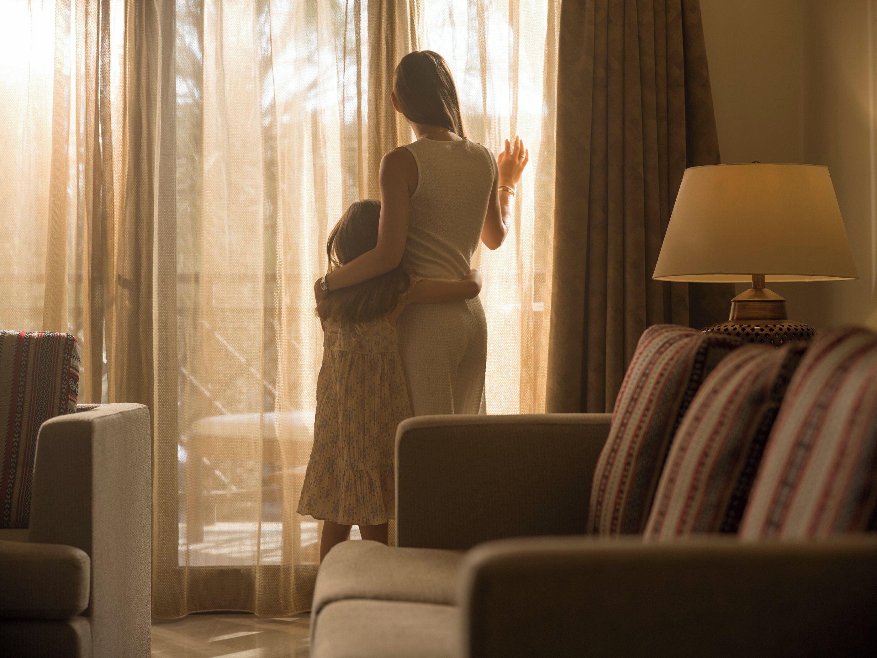 A room with a sofa, a lamp, and a window with sheer curtains.