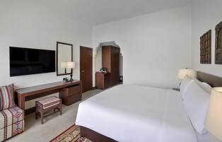 Habitación de hotel con una cama grande, un escritorio con lámpara, televisión y armario.