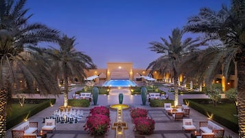 Un área de piscina en un resort, con sillones de descanso, un tablero de ajedrez y palmeras.