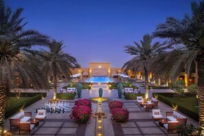 Un área de piscina en un resort, con sillones de descanso, un tablero de ajedrez y palmeras.