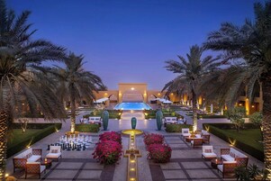 Un área de piscina en un resort, con sillones de descanso, un tablero de ajedrez y palmeras.