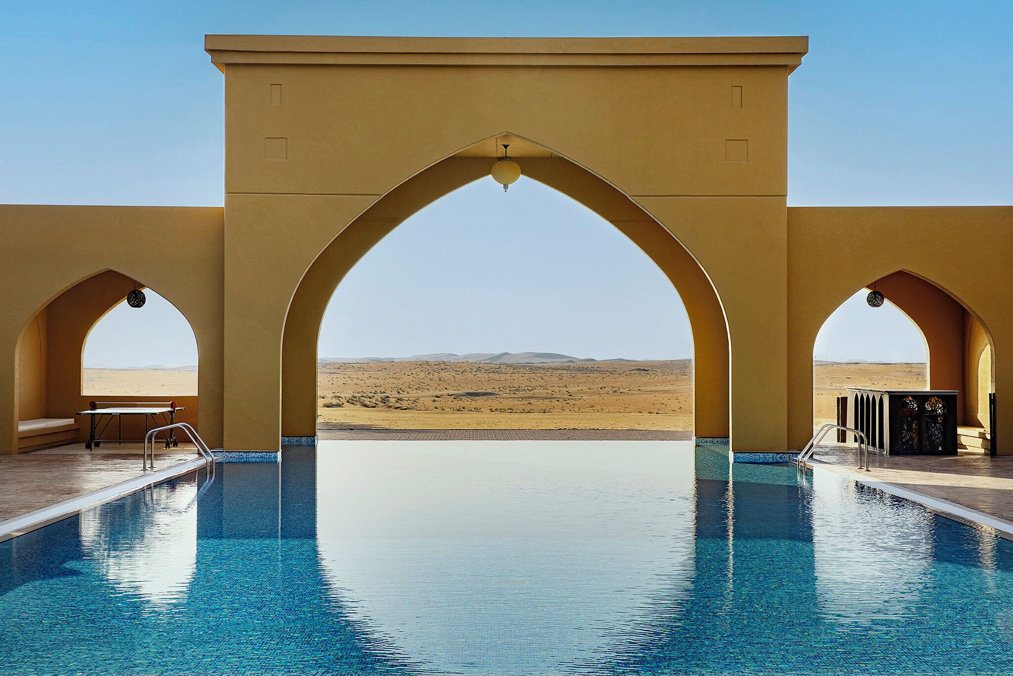 Una piscina con estructuras en arco y vistas al desierto.