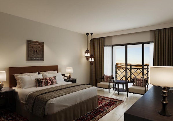 Habitación de hotel con una cama grande, un escritorio con una silla, un balcón con vistas al desierto y un adorno en la pared.