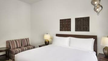 Habitación de hotel con una cama grande, un sofá, dos lámparas de pared y un colgante decorativo.