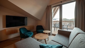 Un salon moderne doté d’un grand téléviseur à écran plat, de deux fauteuils verts, d’un canapé beige et d’une petite table basse en bois.